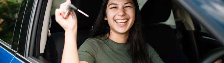 A young woman in the drivers seat of a blue car holding car keys