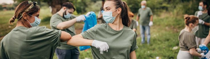 A group collects rubbish in parklands as two women in face masks bump elbows