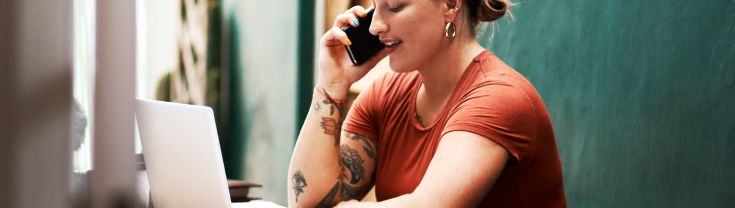 Young businesswoman sitting alone and talking on her mobile phone while using her laptop