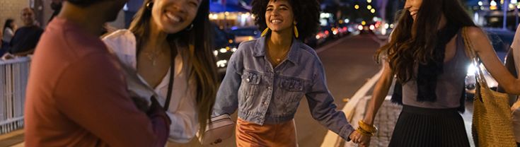 The image features four people walking across a road laughing at night time.