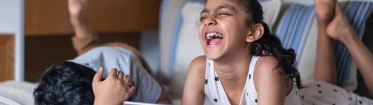 Affectionate primary school age siblings laughing while doing screen time on a tablet computer.