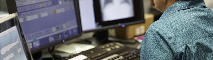 Woman with hand on keyboard looks at central of 3 screens on desk