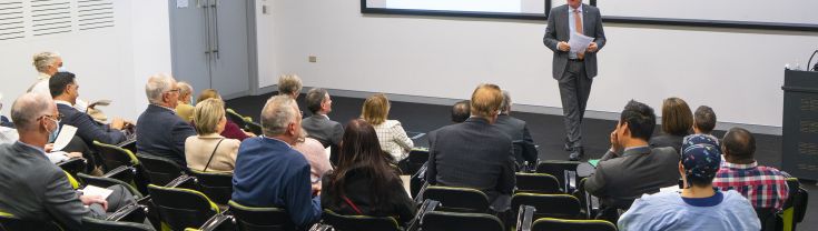 Presenter speaking in front of people in auditorium 