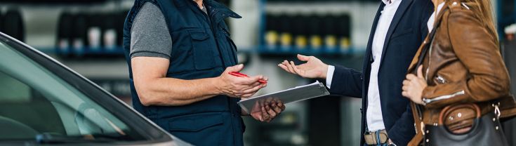 Couple speaking to a car repairer in a workshop