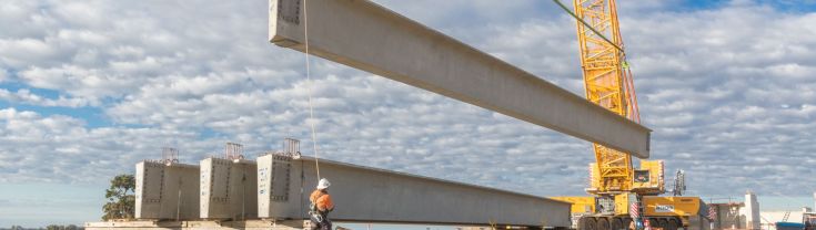 Workperson checks large concrete blocks being moved by giant crane