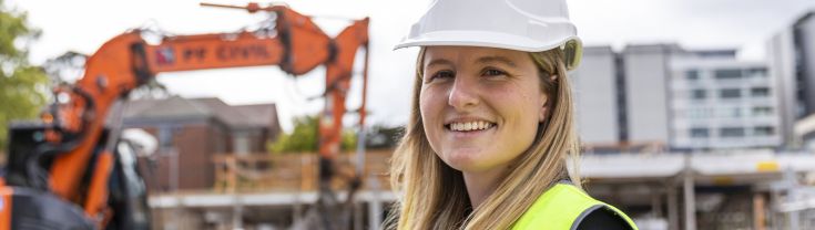 Stephanie is standing on a construction site with a tractor in the background.