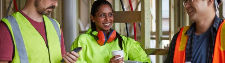 Three different people on a construction site, with one sipping coffee