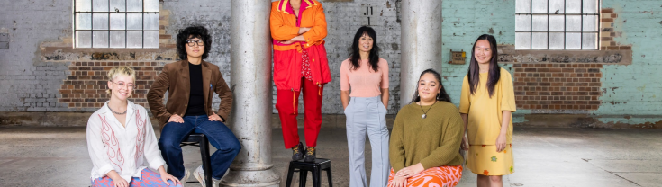 A group of young, colourfully dressed artists pose against interior Carriageworks backdrop.