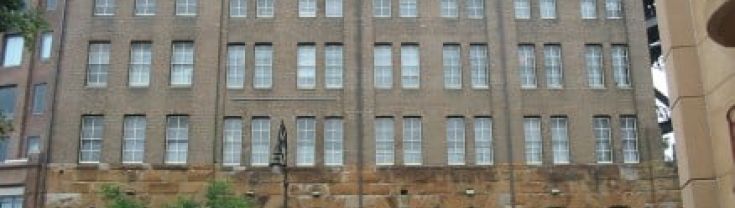 Multi-storey heritage brown brick building with crescent windows near roof.