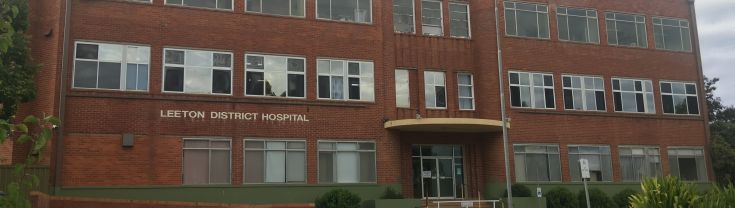 Main entrance to the Leeton Health Service building. The red brick building has a ramp access point to the left of the image and the step leading up to the main entrance to the centre-right of the image. A circular driveway is at the front of the building.