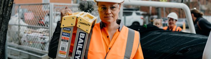 Annie on site in a hard hat carrying a ladder.