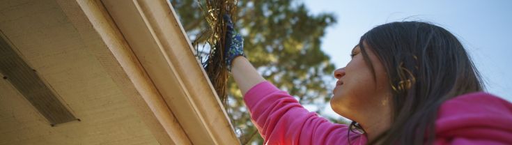 Woman wearing gloves cleaning gutters on a roof