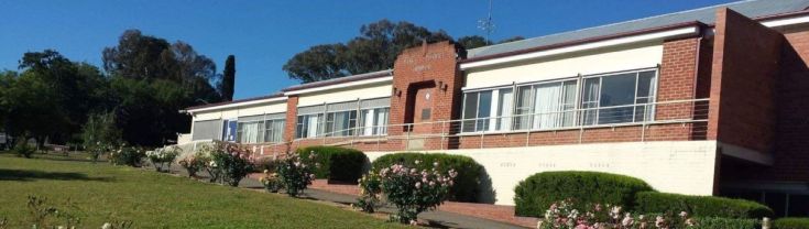 Main entry to the Yass District Hospital. Pink and white rose bushes line the driveway leading to the main entrance, which includes a wheelchair accessible entrance via a ramp. 