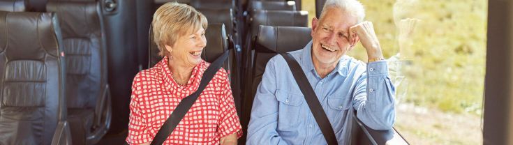 An older man and woman are sitting enxt to each other on a bus laughing.