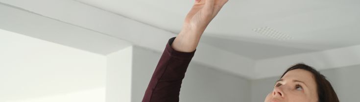 Woman pressing button on ceiling smoke alarm.