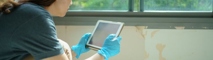 Woman wearing gloves inspecting and photographing paintwork with tablet.