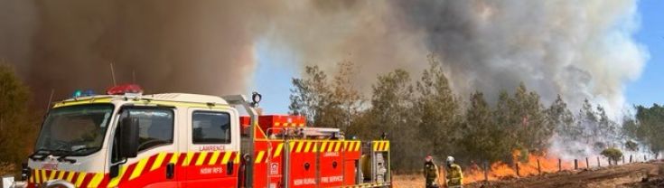 A fire truck next to a grass fire in a paddock