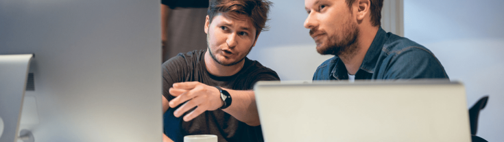 Two people discussing while sitting at computer and laptop