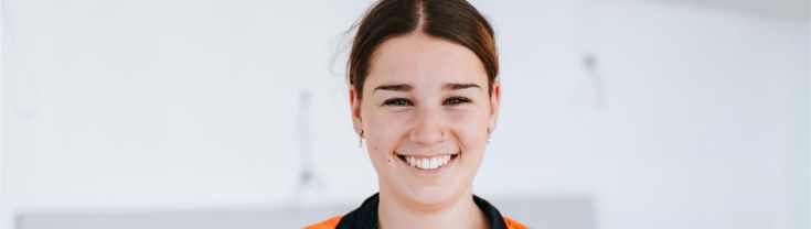 Ashlyn is standing in front of a white wall, wearing hi-vis, smiling. 