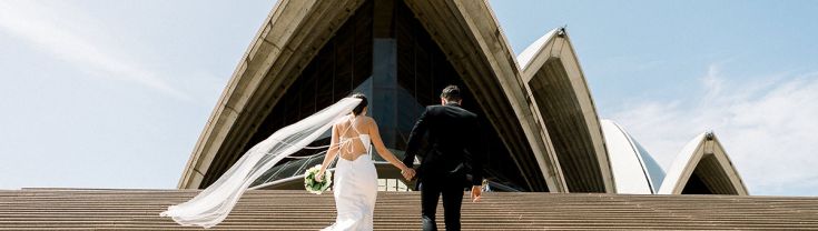 A bride and groom walking up the Sydney Opera House steps. 