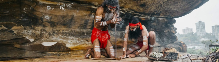 Two Aboriginal men in traditional dress, starting a fire.