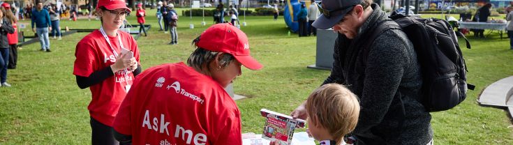 Parramatta Light Rail staff in red shirts and caps talking to a man and child at a community event in Parramatta.