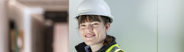 An image of Alice wearing hi vis and a hard hat on a construction site.