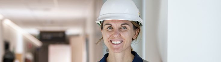 Jess Davis is standing on a construction site in hi-vis with a hard hat on.