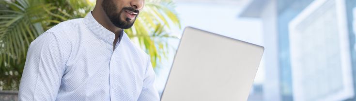 A man sitting outdoors near a home using a laptop.