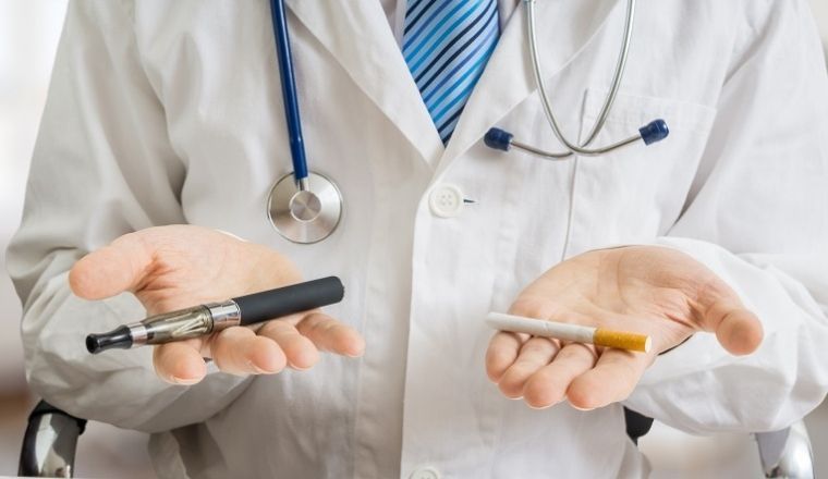 A health worker, gender unknown, holding an e-cigarette in one hand and a tobacco cigarette in the other.