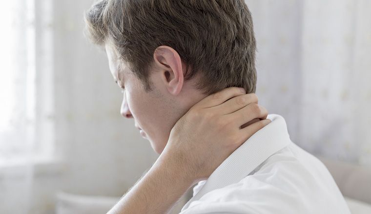 Man in white bedroom with white shirt touching his sore neck profile view