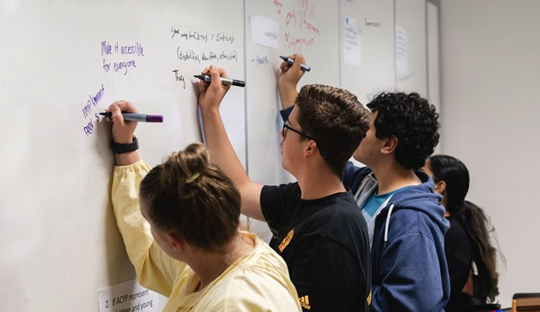 Young people writing on a whiteboard at ACYP office