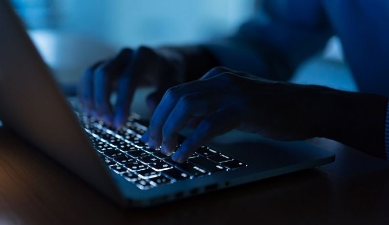 A man typing on a laptop inside a dark room