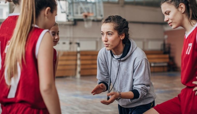 A woman coach talking to two women basketballers on the basketball court.