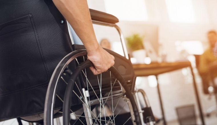 Person's hand steering the wheels of a wheelchair.