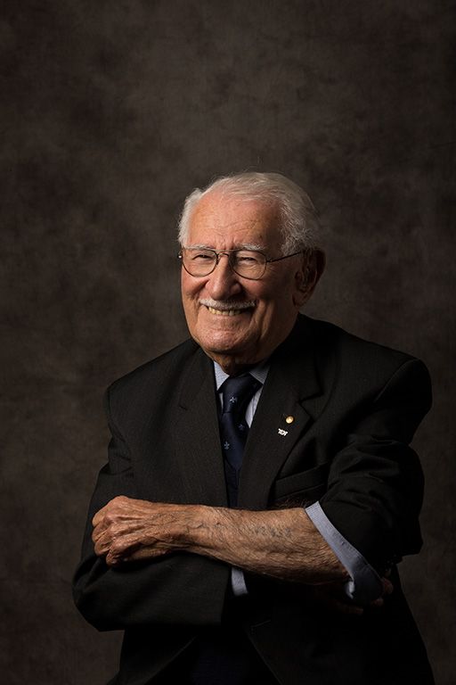 Portrait of Eddie Jaku OAM sitting in a suit with a brown background