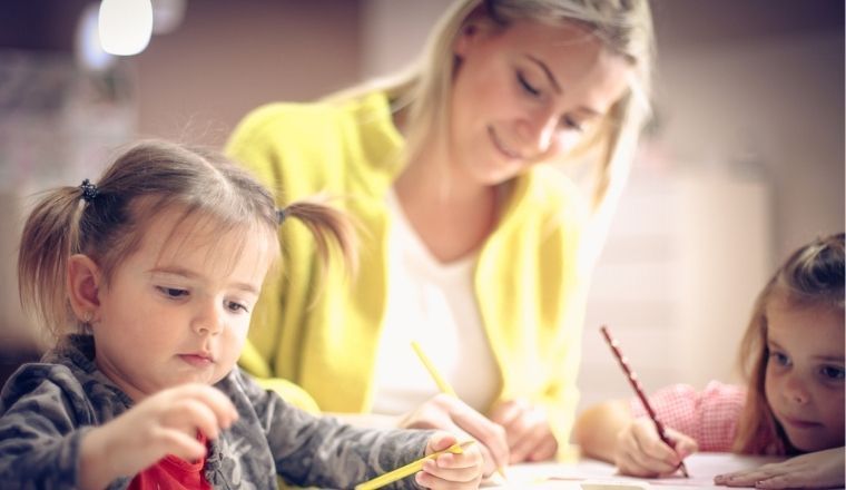 A woman and two young girls drawing together.