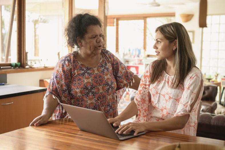 Two women talking and working on a laptop