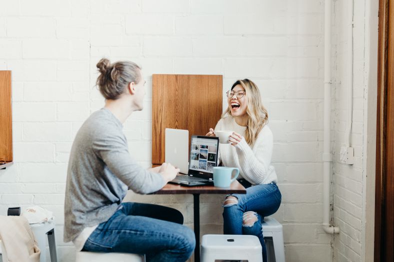 Two people seated having coffee together with a laptop