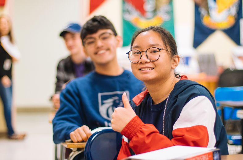 Teenage girl in a classroom gives a thumbs up gesture