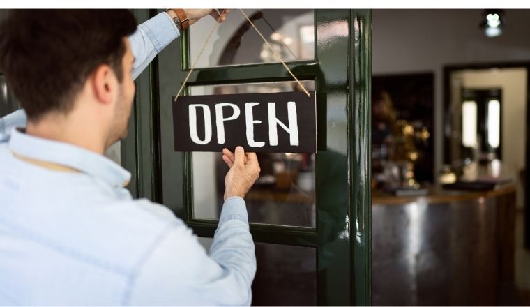 Male restaurant owner hanging an open sign on a door.