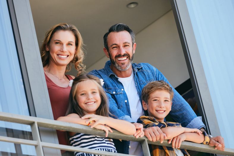 A mother, father and two children looking out a balcony apartment window