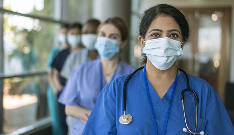 Group of women in scrubs and masks stand in a hospital looking at the camera.