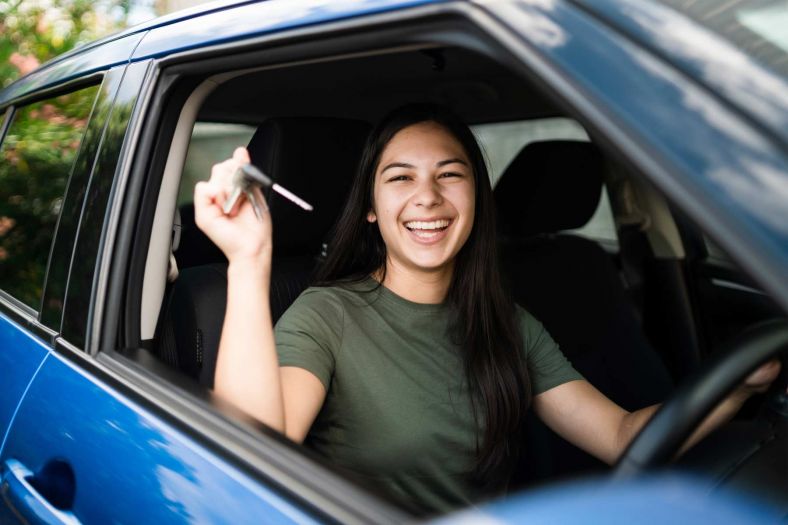 A young woman in the drivers seat of a blue car holding car keys