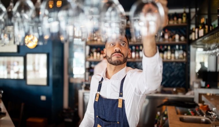 A bartender taking a wineglass from the overhead rack at a bar counter.