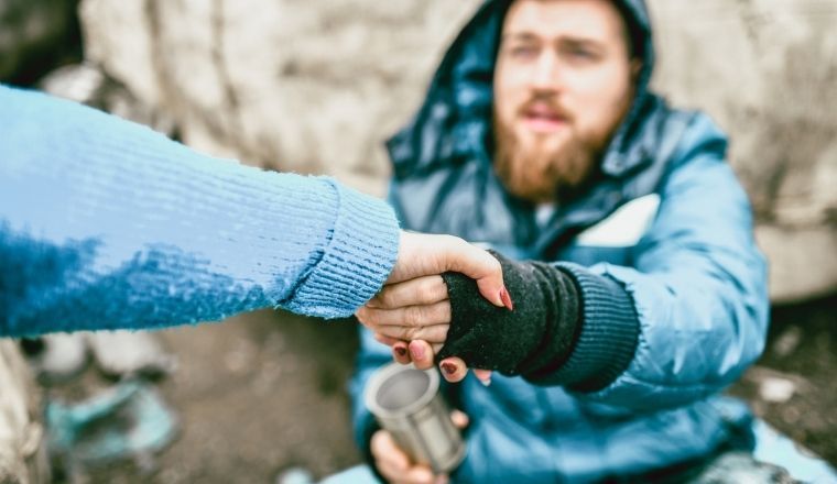 A homeless man on the street getting help from a woman.