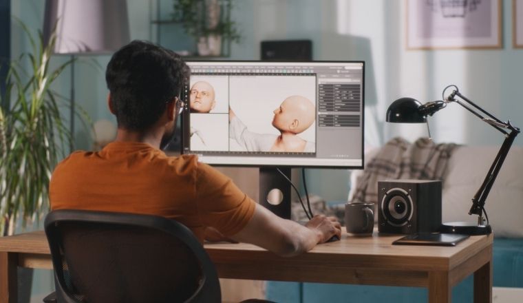 Behind view of a man sitting at a desk, creating an animated character on a computer screen.