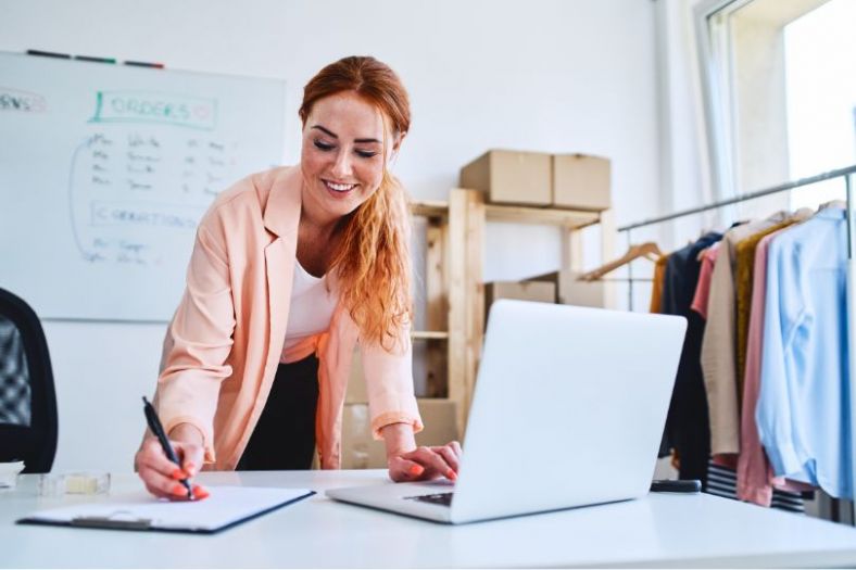 A female business owner at work at a desk with clothes in the background