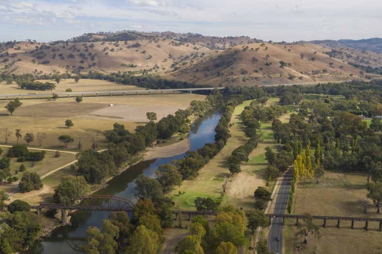 An Aerial shot overlooking the Murrumbidgee River and rural Gundagai. The image includes expansive landscape, a winding river, a bridge over the river and two large roadways winding through the countryside. 