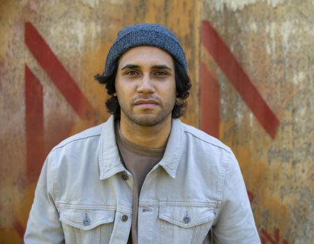 A young man wearing a beanie, standing near a wall